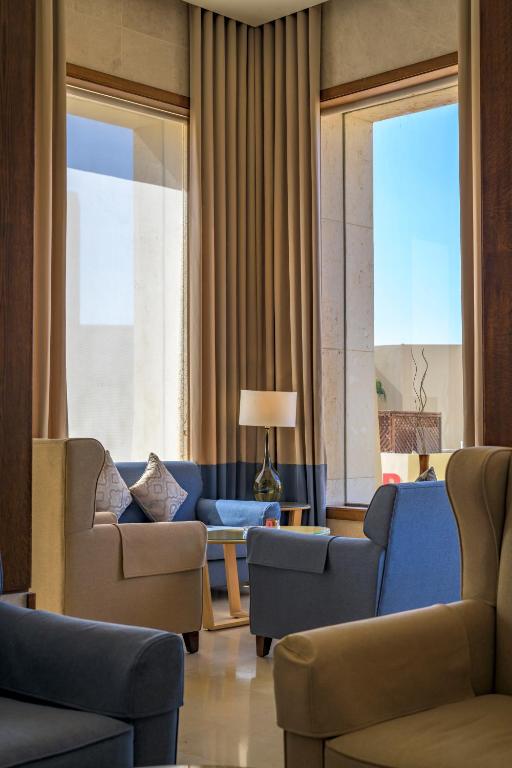 Mūsdienīga dzīvojamā telpa ar ērtām krēslām, galds un lampa, kas rada mierīgu atmosfēru. Lielie logi nodrošina dabisko apgaismojumu un skatu uz ārpusi.