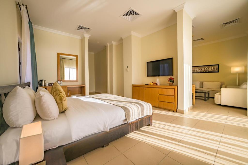 Gaiša un moderna viesnīcas numura iekārtojums ar ērtu gultu, televizoru un atpūtas zonu. Telpā ir lieli logi, kas nodrošina dabīgu apgaismojumu.