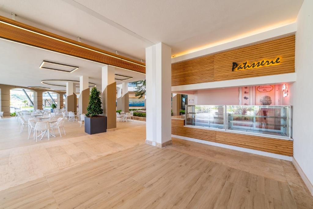 Moderns kafejnīcas interjers ar elegantām mēbelēm, kas ietver ēdamgaldu un krēslus, kā arī konditorejas stendi ar saldumiem. Gaisma un dekoratīvie elementi piešķir telpai patīkamu atmosfēru.
