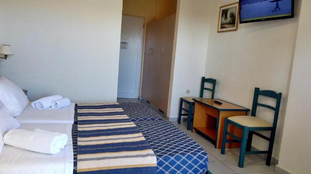 Gaiša viesnīcas istaba ar divām gultām, televizoru pie sienas un nelielu galdu ar krēsliem. Gultas rotā balti dvieļi, bet grīda ir flīzēta.