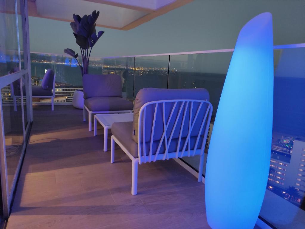 Mūsdienīga balkona telpa ar ērtām mēbelēm un stilīgu apgaismojumu, kas rada relaksējošu atmosfēru. Skats uz pilsētu un jūru pie vakara gaismas.