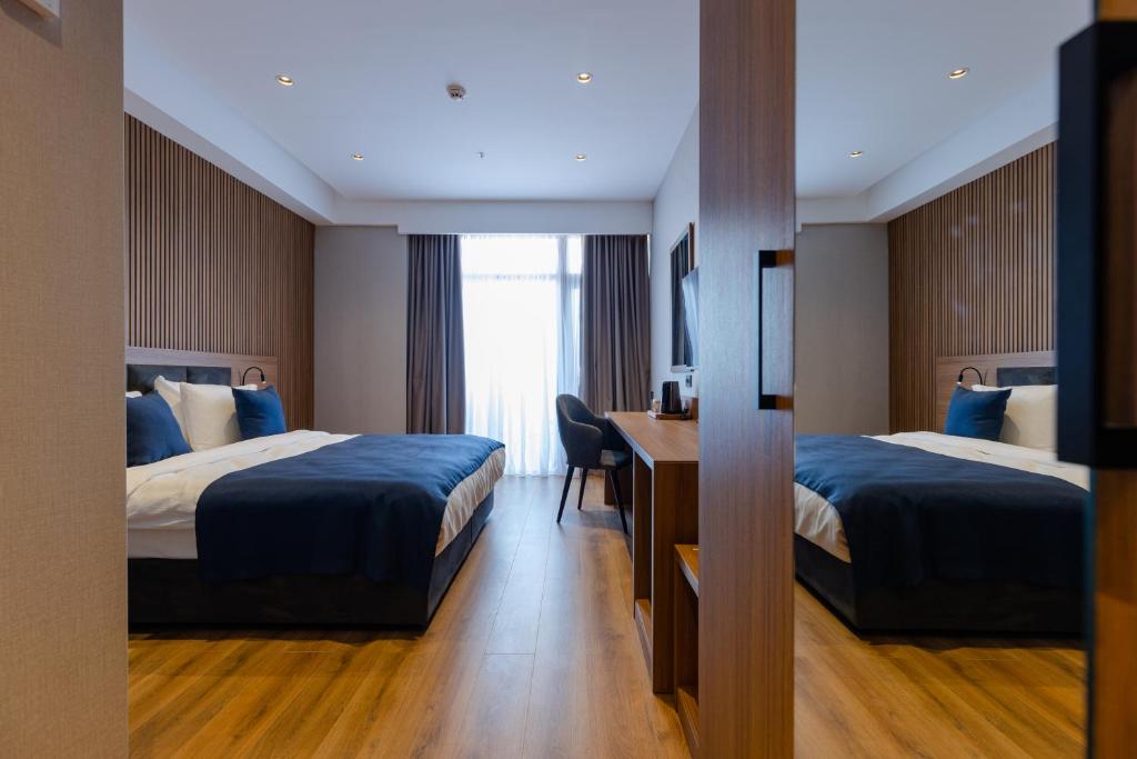 Mūsdienīga viesnīcas numura iekšskats ar divām gultām, koka grīdu un logu, kas sniedz dabisko apgaismojumu. Interjers ir iekārtots ar mierīgu krāsu paleti un modernām mēbelēm.