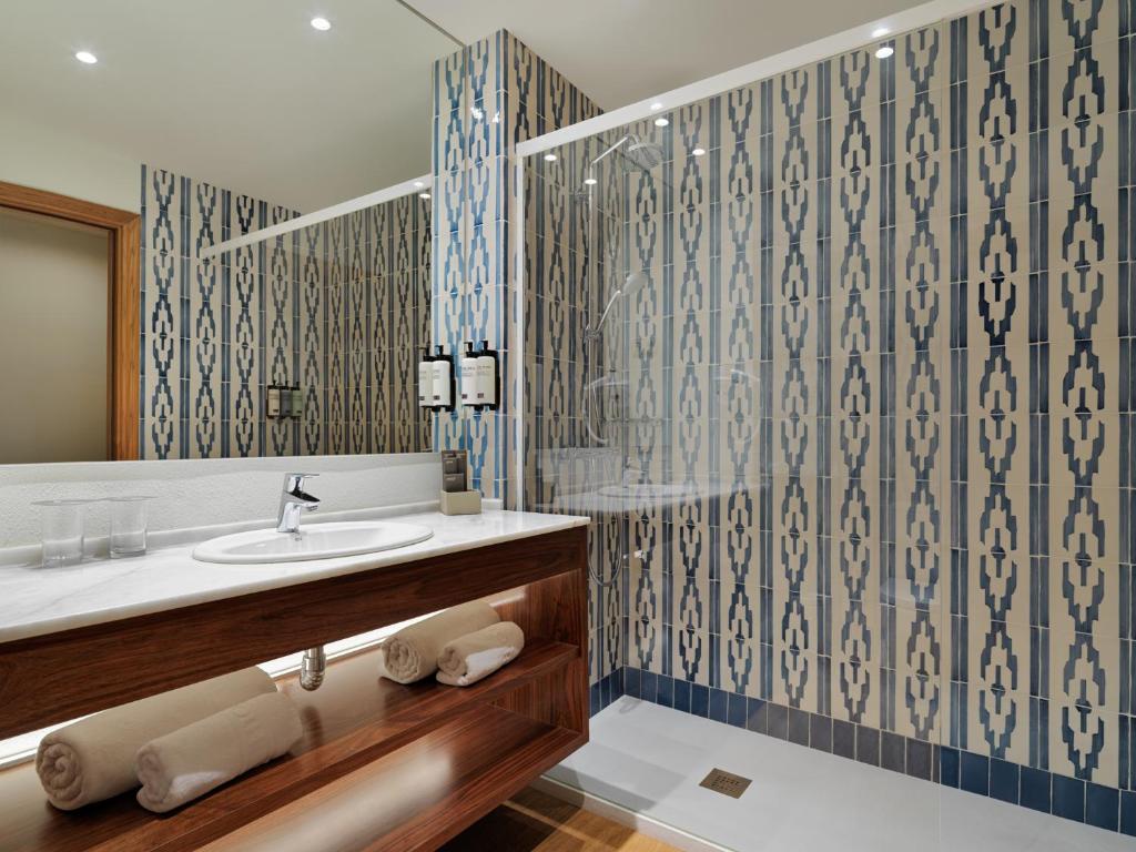 Mūsdienīgs vannas istabas interjers ar dekoratīvām flīzēm, koka izlietni un elegantu apgaismojumu. Iekārtota ar dvieļiem un higiēnas līdzekļiem.