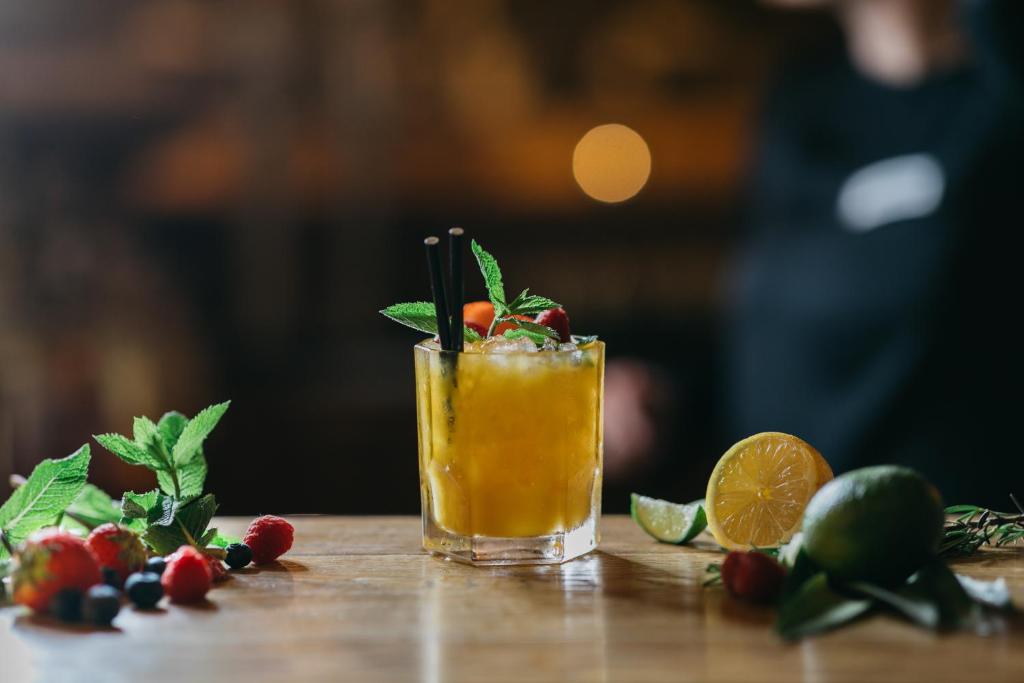 Aromātisks kokteilis ar melleņu un aveņu dekoru, pasniegts glāzē uz koka galda, blakus svaigiem augļiem un piparmētru lapām.