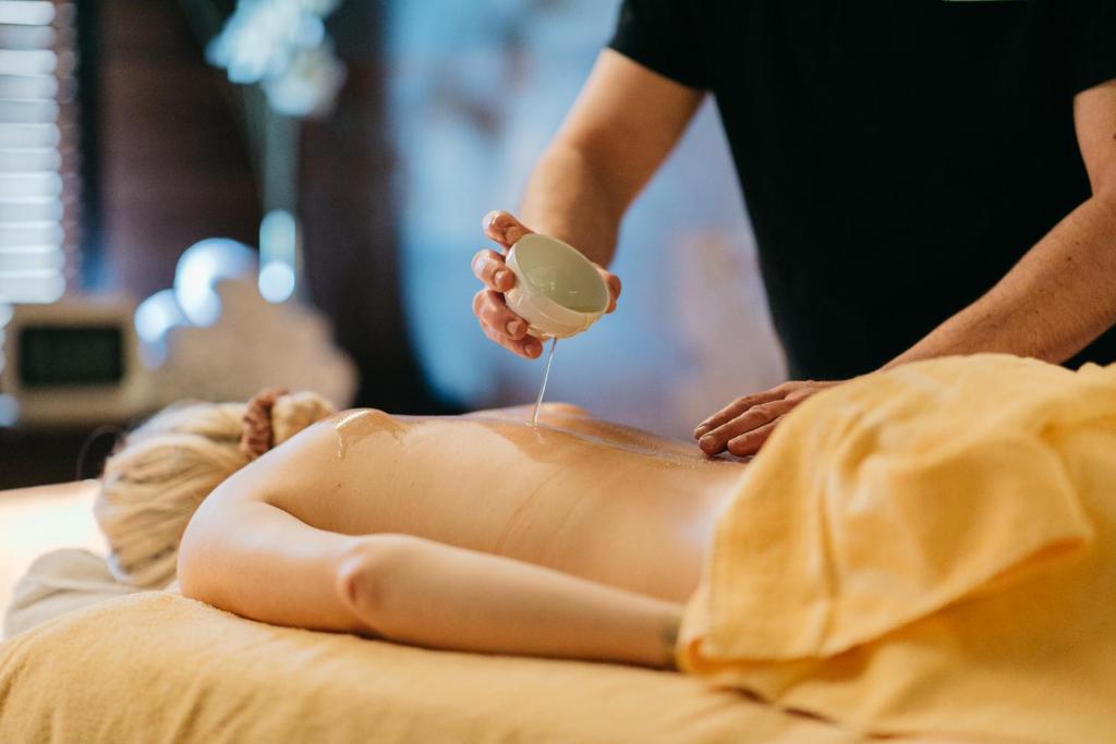 Masāžas sesija, kur masieris uzklāj eļļu uz klienta muguras relaksējošā vidē.