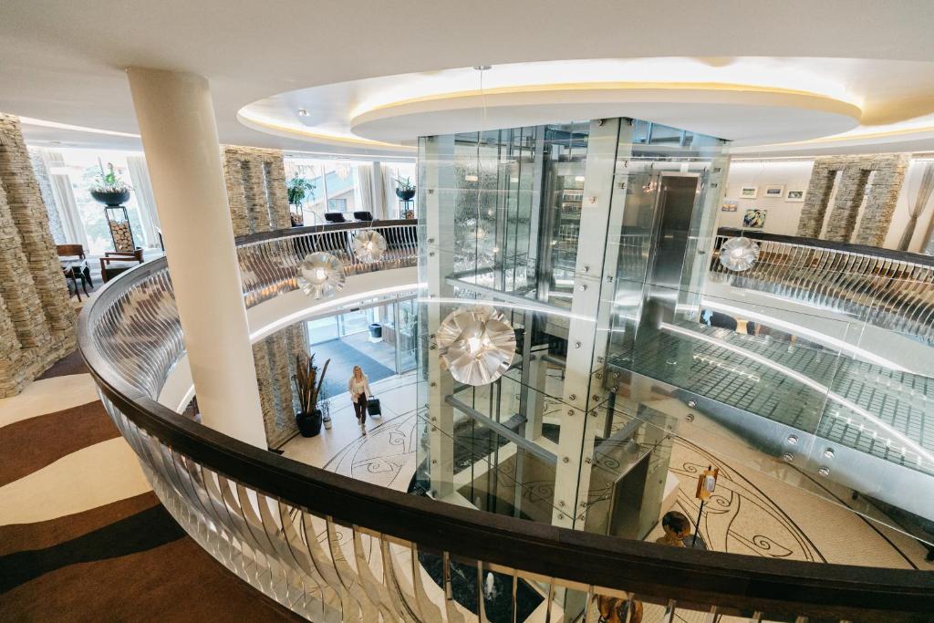 Mūsdienīgs viesnīcas vestibils ar elegantu dizainu, stikla liftu un modernām dekorācijām, kas rada gaisīgu un plašu atmosfēru.