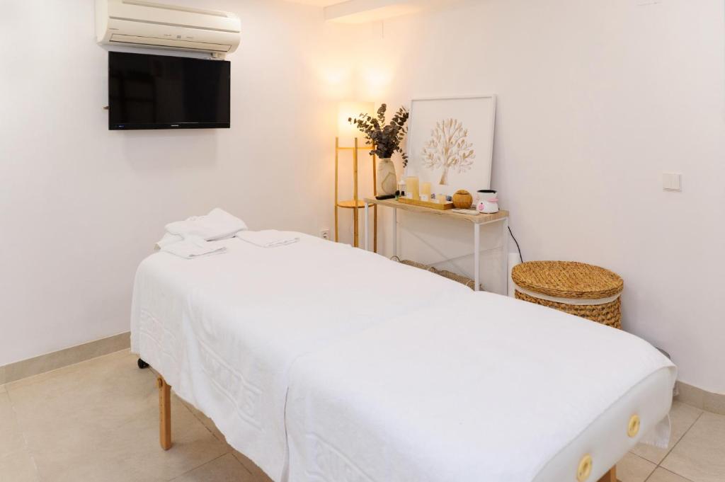 Mūsdienīgs masāžas kabinets ar baltu gultu, televizoru un dekoratīvām augu kompozīcijām. Telpai ir gaiša apgaismojuma atmosfēra, kas veicina relaksāciju.