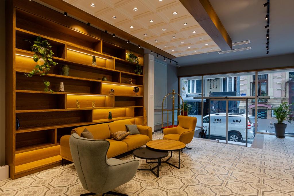 Mūsdienīga viesnīcas uzgaidāmā telpa ar elegantu dīvānu, krēslu un stilīgu plauktu, kurā redzami dekoratīvi elementi un augi. Telpa ir gaiša un gaumīgi iekārtota, radot komfortablu atmosfēru.