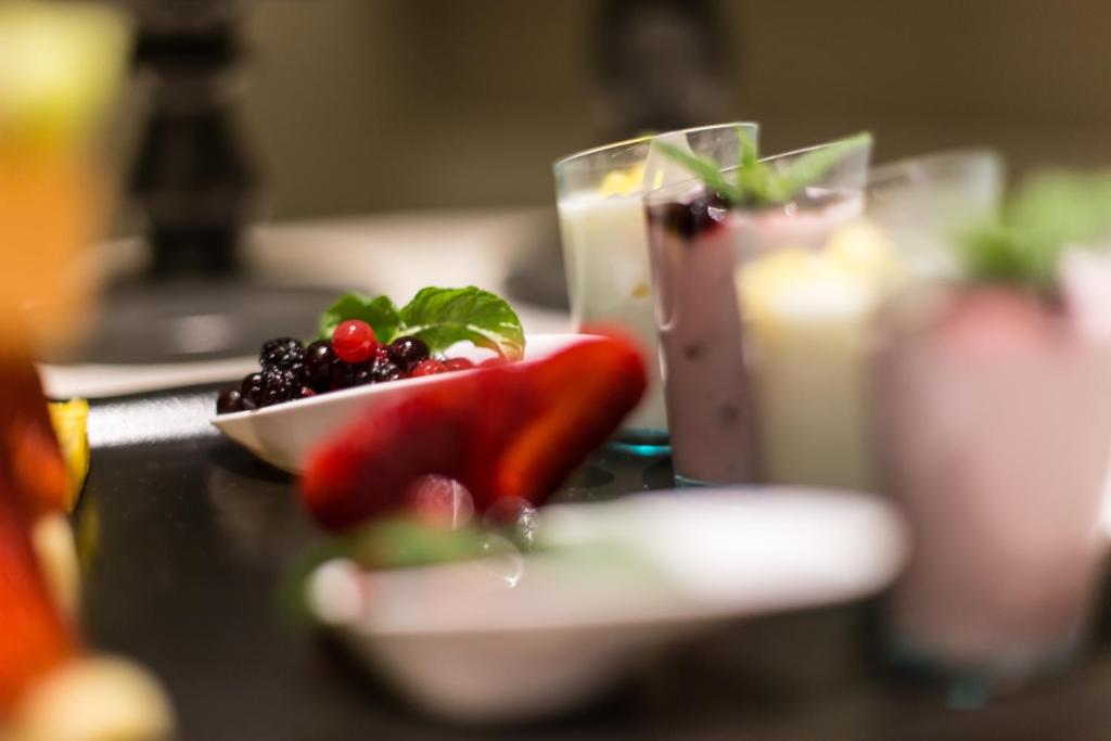 Krāsaini dzērieni un augļi uz galda, tostarp dažādi augļu kokteiļi un ogas. Mintes lapiņas piešķir svaigumu un garšas daudzveidību.