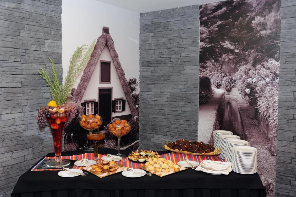 Svētku galds ar dažādiem ēdieniem un dzērieniem, fons ar melnbaltu attēlu un tradicionālu māju. Galds dekorēts ar augļiem un uzkodu šķīvjiem.