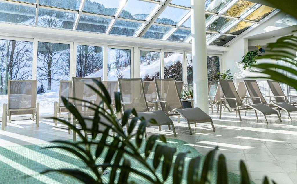 Saulainā atpūtas telpa ar logiem līdz grīdai, kas piedāvā skatu uz sniegotu ainavu. Telpā ir vairākas atpūtas krēsli un augu elementi, radot mierīgu atmosfēru.