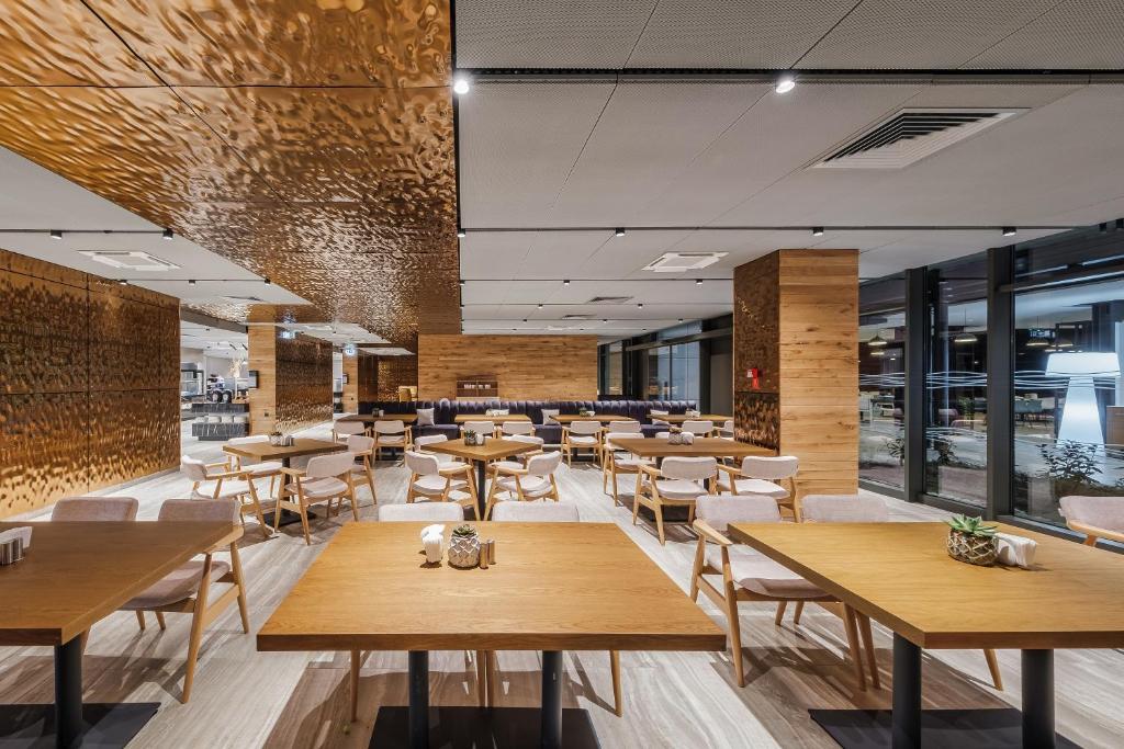 Mūsdienīgs restorāna interjers ar koka mēbelēm un elegantu apgaismojumu, radot siltu un aicinošu atmosfēru. Platība ir plaša, ar daudzām ērtām vietām pie galdiem.