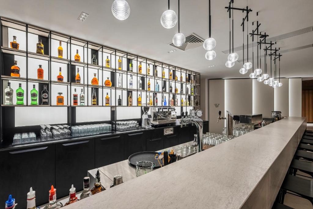 Mūsdienīgs bārs ar elegantu dizainu, kas piedāvā plašu alkohola dzērienu izvēli un stilīgu apgaismojumu. Bāra plauktos redzami dažādi dzērieni, kas piešķir atmosfēru.