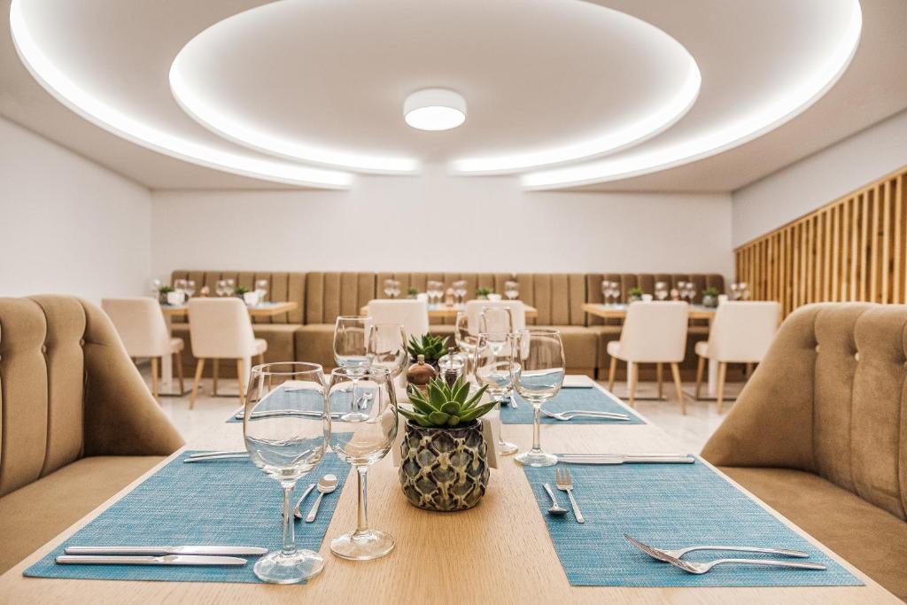 Mūsdienīgs restorāns ar elegantu interjeru, kurā ir koka elementi un minimālistisks dizains. Galdi ir saklāti ar zilu galdautu un glāzēm, radot patīkamu atmosfēru.