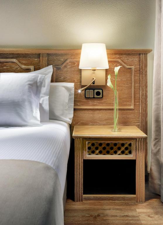 Gultas apgaismojums ar koka galvgali un naktsgaldiņu, uz kura ir zieds. Elegantā viesnīcas interjēra elements.