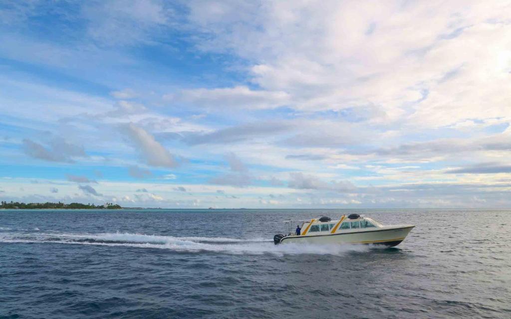 Ātrā laiva pārvietojas pa zilo ūdeni zem skaidra debesīm. Skats uz jūru ar zāļu salām tālumā.