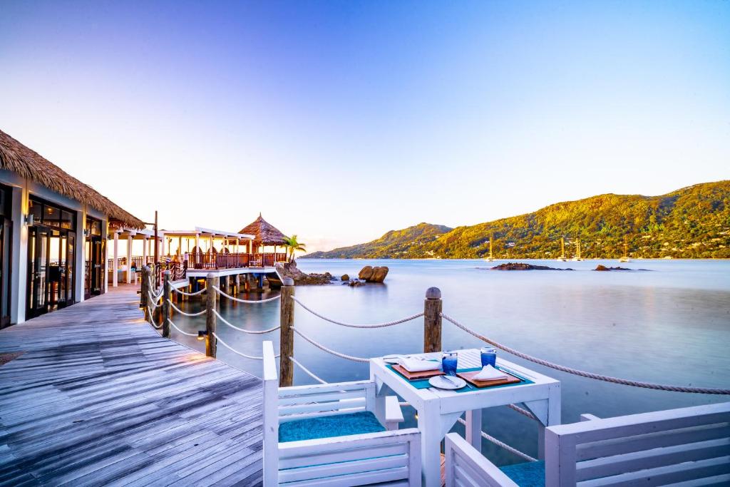 Romantisks skats uz pludmali ar koka molu un ēdināšanas galdu, kas atrodas pie ūdens, apkārt gleznainām kalnu ainavām.