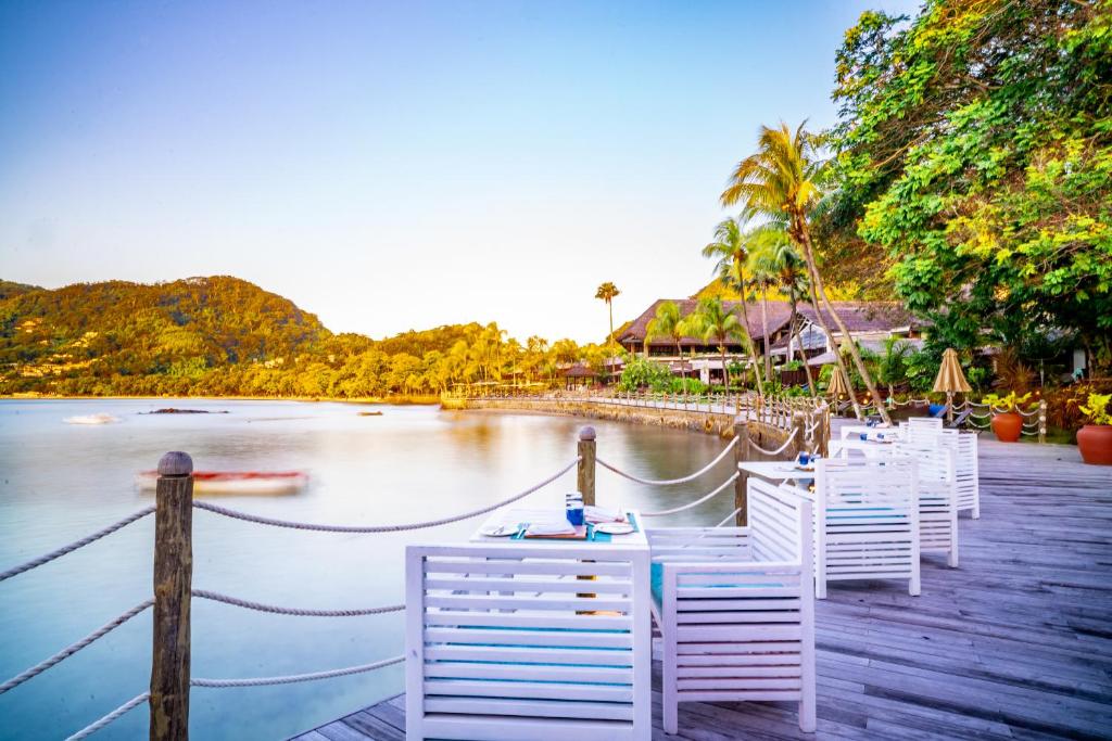 Relaksējošs skats uz piekrasti ar terasi un palmām, kas iestieptas virs ūdens. Ideāla vieta mierīgai atpūtai un dabas baudīšanai.