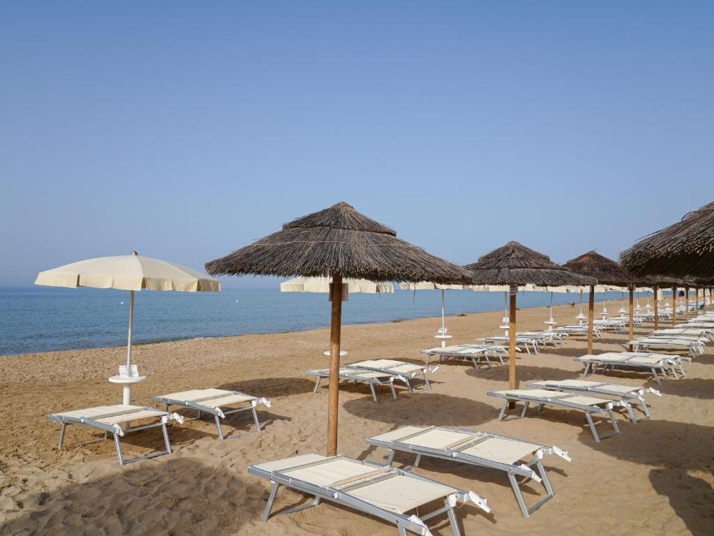 Pludmales skats ar saulessargiem un atpūtas krēsliem, kas izvietoti smiltīs pie ūdens. Klusa atmosfēra un skaidrs debesis rada relaksējošu noskaņu.