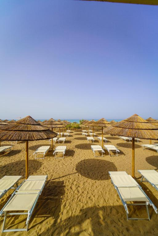 Pludmales ainava ar saulessargiem un pludmales krēsliem smilšu uzklājumā, ar jūru fona.