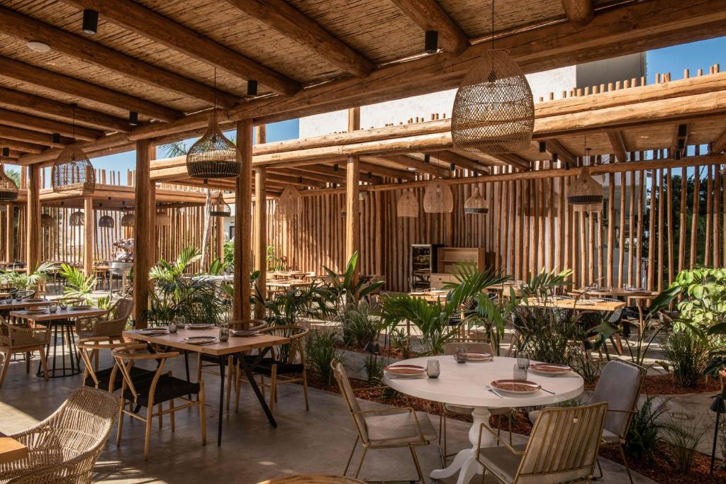 Moderns restorāna interjers ar koka konstrukcijām, augu dekorācijām un elegantiem galdiem, radot patīkamu un relaksējošu atmosfēru.