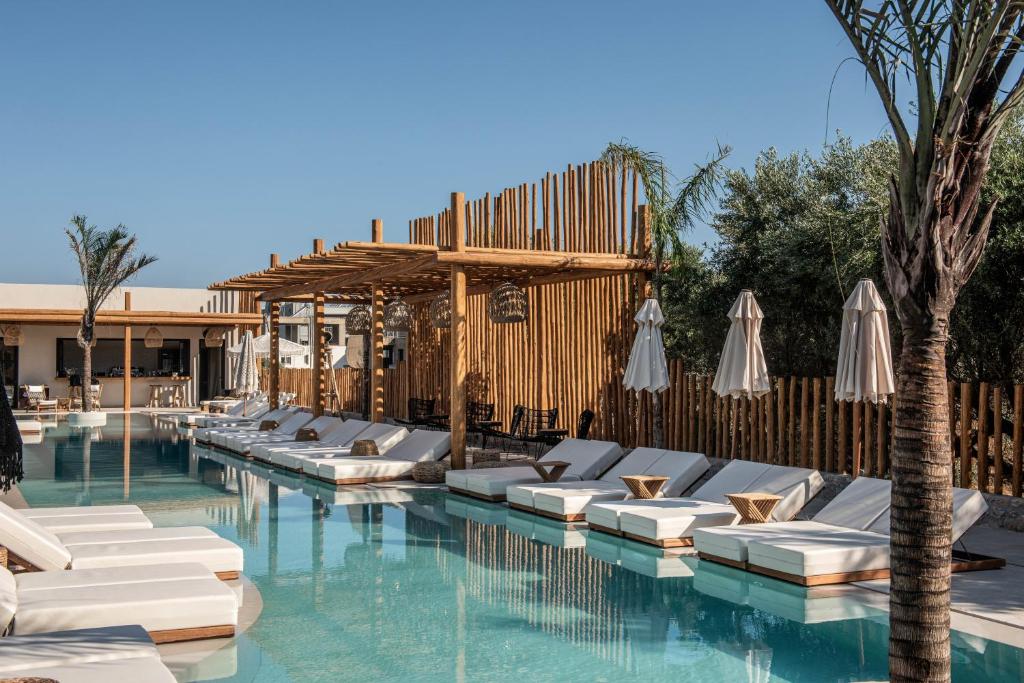 Elegantična atpūtas zona pie baseina ar sauļošanās krēsliem un dabīgām palmām, kas rada relaksējošu atmosfēru. Koka konstrukcijas un gaišas krāsas akcentē modernu dizainu.