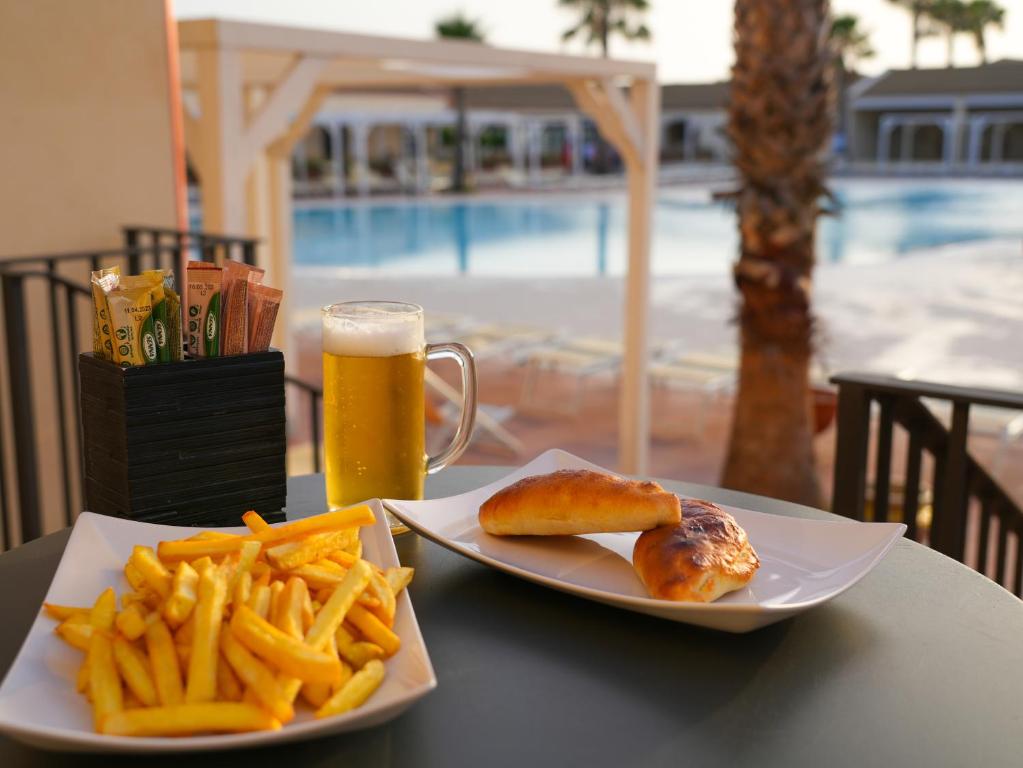 Frī kartupeļi, alus un pīrādziņi uz galda pie baseina, ar palmām fona. Ideāla atpūtas brīža atmosfēra.
