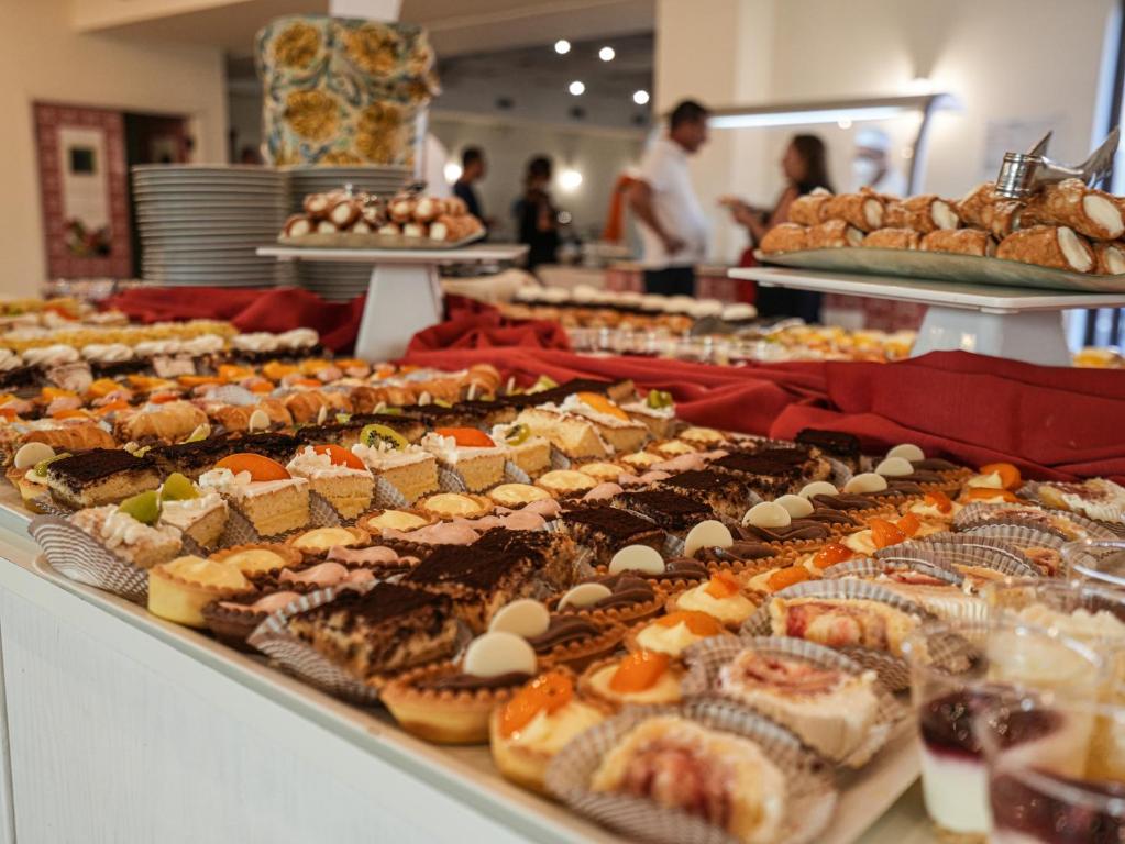 Deserts izkārtojums ar dažādām kūkām un saldumiem uz galda, kas ir dekorēts ar sarkanu audumu. Fons satur cilvēkus un citas saldumu šķirnes.