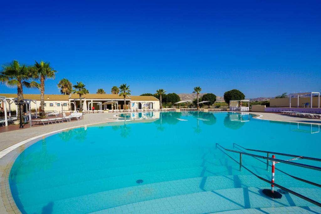 Lieliska peldbaseina ainava ar palmām un skaidru zilo debesu fonu, radot relaksējošu atmosfēru. Ideāla vieta atpūtai un izklaidei.