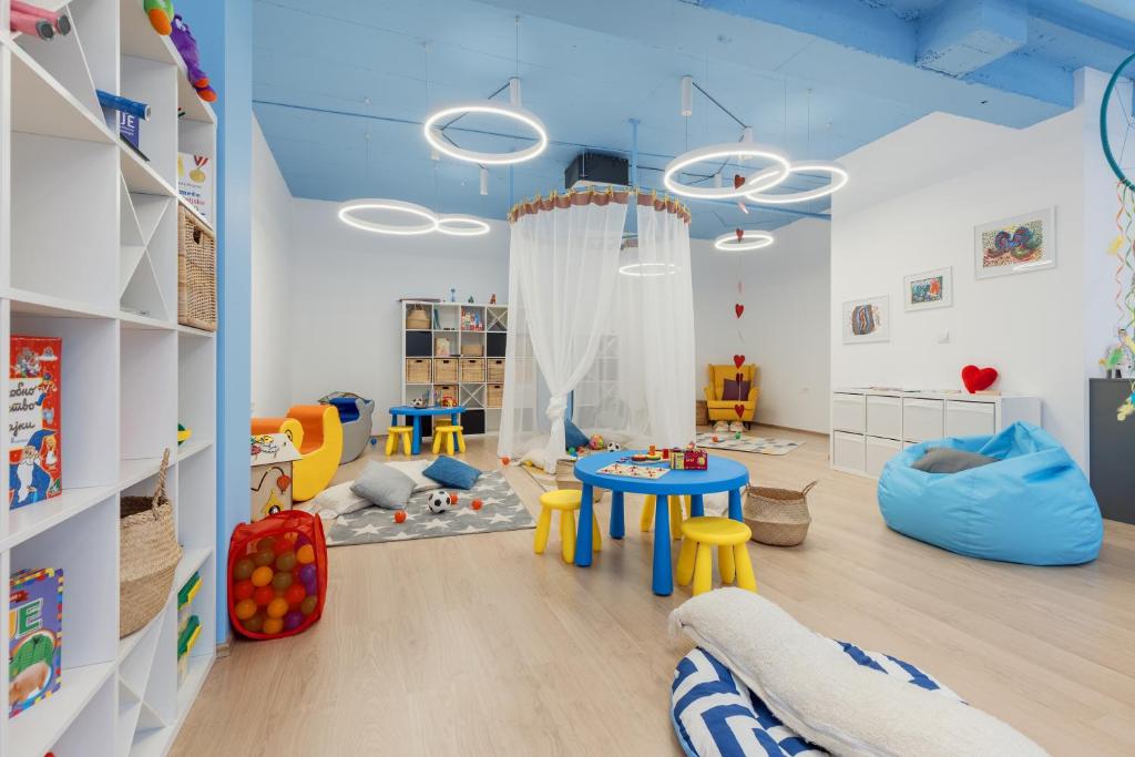 Bērnu rotaļu istaba ar spilgtām krāsām, rotaļlietām un ērtām sēdvietām, kas veidota draudzīgai un izglītojošai videi. Gaismas un dekorācijas rada patīkamu atmosfēru bērnu spēlēm un radošām aktivitātēm.