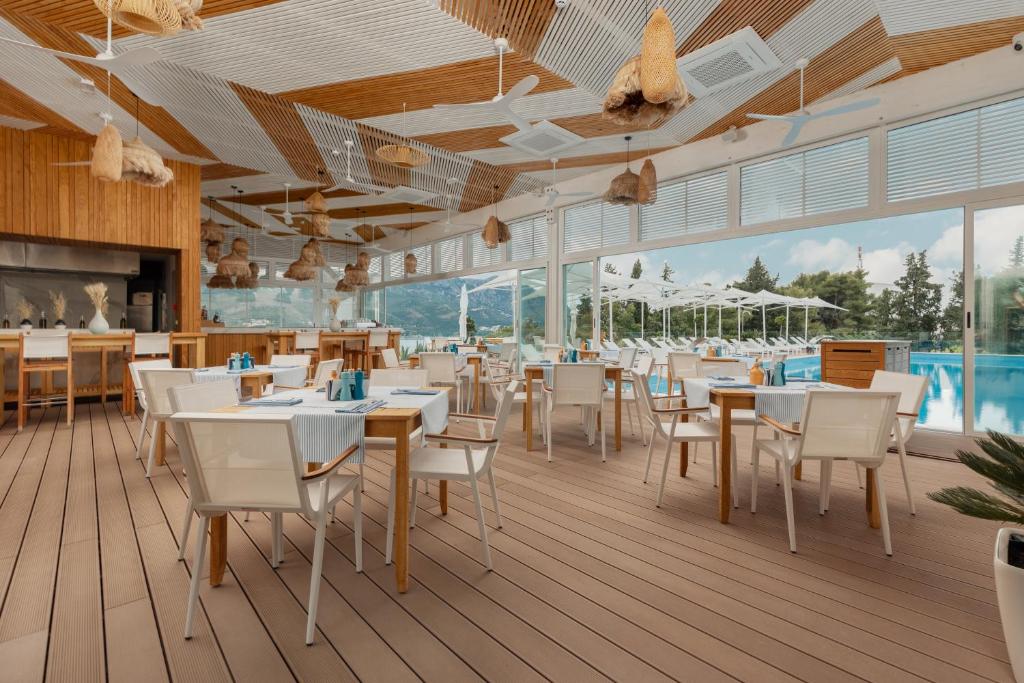 Moderns restorāns ar koka interjeru un plašiem logiem, kas piedāvā skatu uz baseinu. Galdi ir sakārtoti ar baltām galdautām un dekoratīviem elementiem.