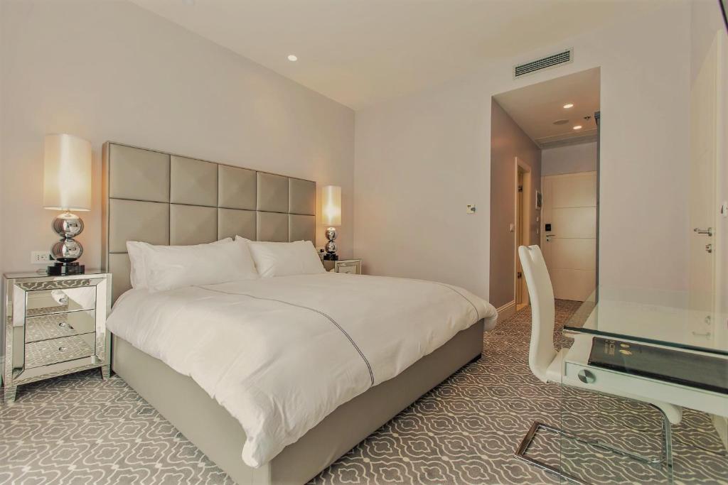 Mūsdienīga guļamistaba ar plašu gultu, elegantiem spoguļiem un stilīgu rakstu grīdu. Telpa ir gaiša un ērta, radot relaksējošu atmosfēru.