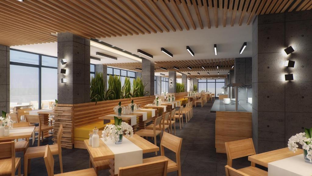 Mūsdienīgs restorāna interjers ar koka elementiem un lieliem logiem, kas nodrošina dabīgu apgaismojumu. Galdi ir dekorēti ar ziediem, radot patīkamu atmosfēru.
