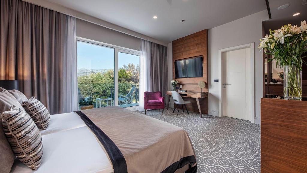 Mūsdienīga viesnīcas numura iekšskats ar plašu logu, ērtu gultu un stilīgu mēbeļu izkārtojumu. Numurā ir televizors un dekoratīvas ziedu kompozīcijas.