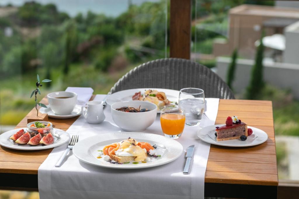 Brokašu galda klāšana ar dažādiem ēdieniem, tostarp smalkmaizītēm, augļiem, kafiju un sulām, baudot skaistu ainavu.