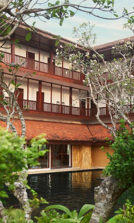 Mūsdienīgs viesnīcas komplekss ar kāpņu telpu un balkoniem, ko ieskauj zaļa daba un ūdens baseins. Relaksējoša atmosfēra, kas aicina uz atpūtu.