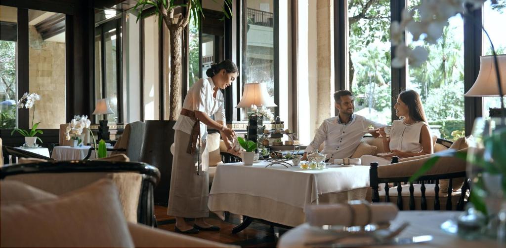 Elegants restorāns ar komfortablu iekārtojumu, kur viesi izbauda maltīti, kamēr apkalpojošais personāls rūpējas par viņu vajadzībām. Gaisīga atmosfēra ar zaļajiem augiem un dabīgu apgaismojumu.