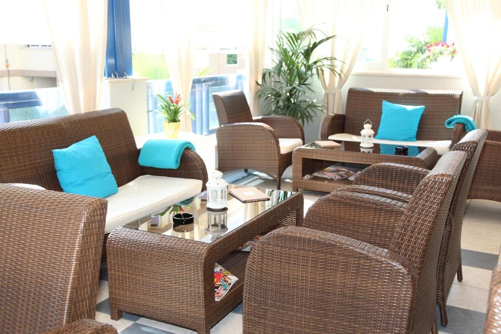 Mūsdienīgs viesistabas interjers ar brūniem rattan mēbeļu komplektiem, ko papildina zilas spilvendrānas un dekoratīvi augi. Gaisīgs un ērts telpas dizains ar stikla galdu un dabisku apgaismojumu.