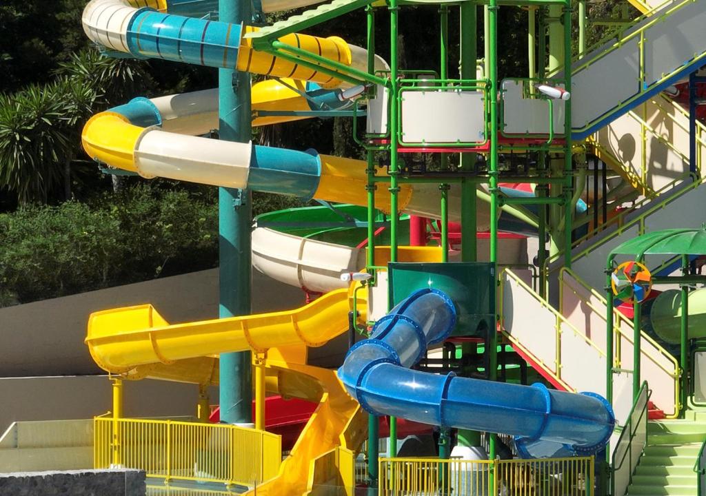 Krāsainie ūdens slidkalniņi atrakciju parkā, kas piedāvā jautrību un izklaidi ģimenēm un bērniem. Slidkalniņi ir dažādu krāsu un formu, veidojot pievilcīgu ainavu.