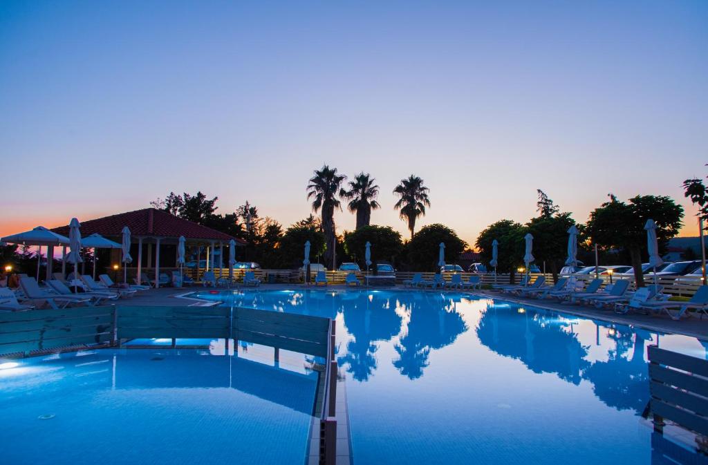 Vakarā apgaismota baseina zona ar palmām un atpūtas krēsliem, radot mierīgu un relaksējošu atmosfēru. Ideāla vieta atpūtai pie ūdens.