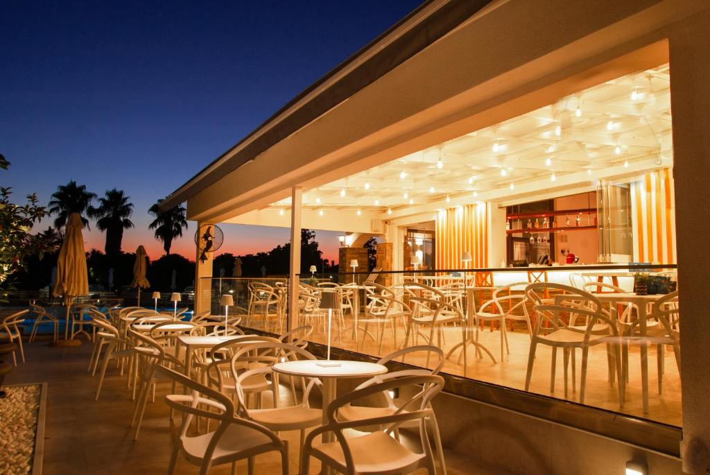 Āra restorāna terase ar apgaismojumu un baltiem galdiem saulrieta gaismā. Romantiska atmosfēra ar palmām fona.