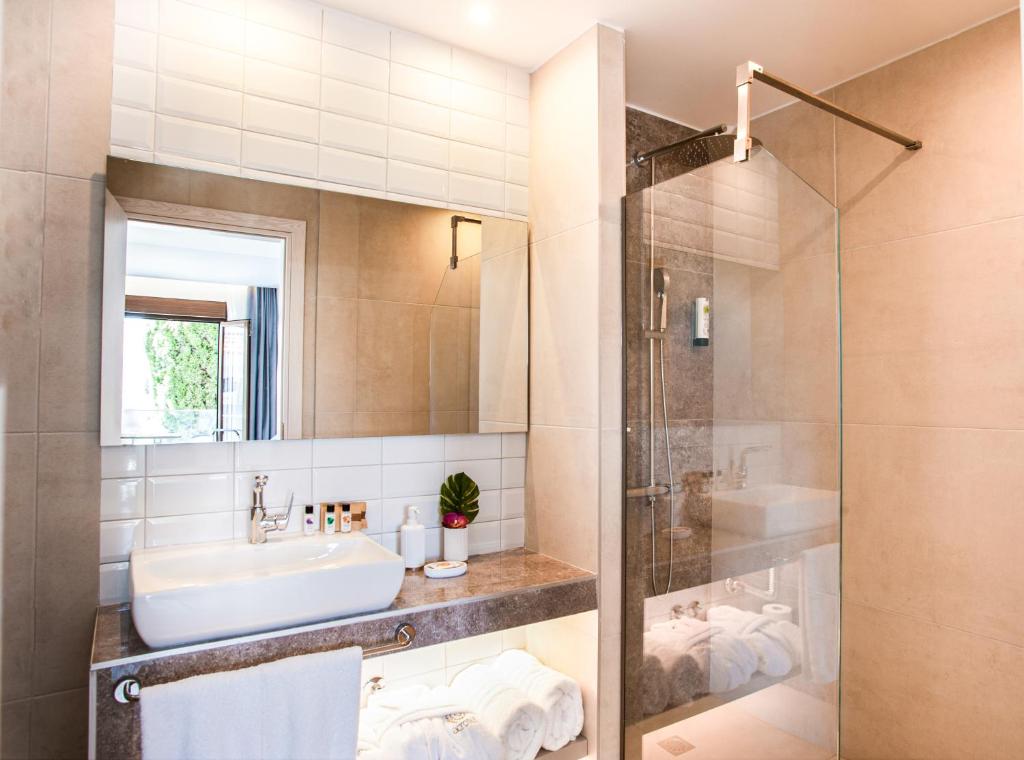 Moderna vannas istaba ar stikla dušu un elegantu izlietni, kas papildināta ar dabīgiem elementiem un gaismas avotiem.