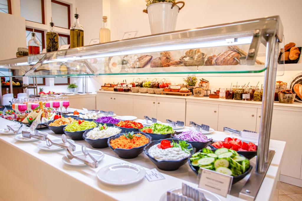 Bagātīgs salātu bārs ar dažādām dārzeņu un garnīru opcijām, izkārtots modernā restorānā. Uz galda redzami krāsaini dārzeņu salāti, dzērieni un maizītes.