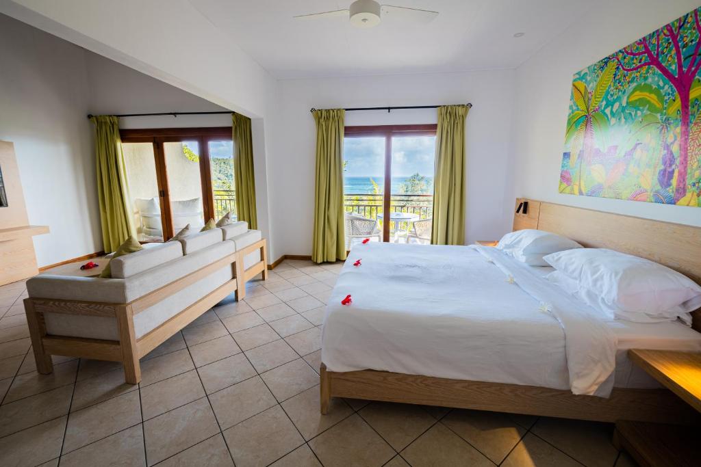 Mūsdienīgs viesnīcas numurs ar skatu uz jūru, kurā ir ērta gulta, dīvāns un krāsainas gleznas uz sienas. Interjers ir gaišs un viesmīlīgs, nodrošinot relaksējošu atmosfēru.