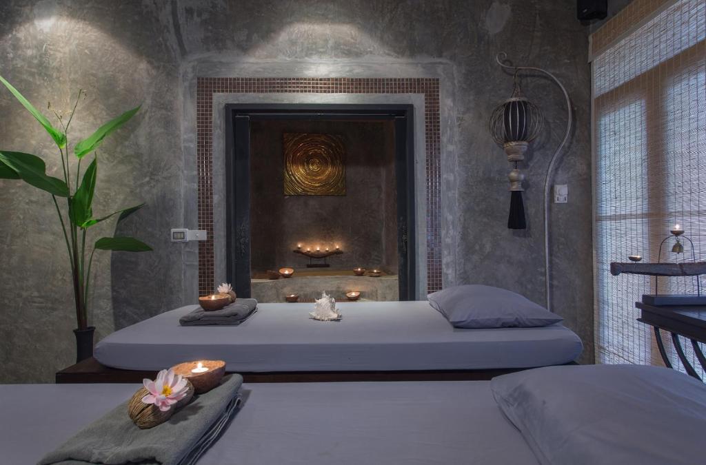 Mierīga spa telpa ar divām masāžas gultām, dekorētām ar ziediem un sveču gaismu, fonā redzama relaksējoša atmosfēra un augu elementi.