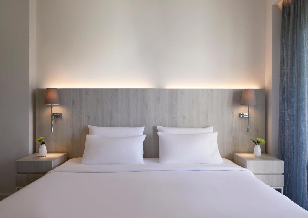 Mūsdienīga guļamistaba ar ērtu gultu un koka galvgali, ko apgaismo silta gaisma, blakus ir eleganti naktsgaldiņi ar lampām un puķu kompozīcijām.