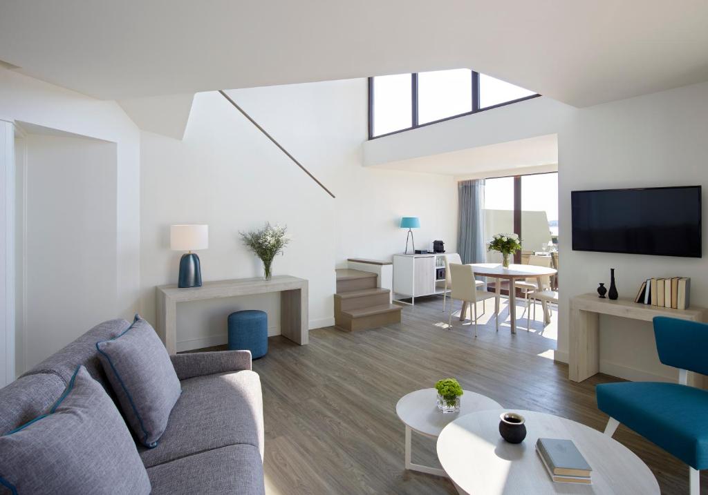 Mūsdienīgs un gaišs viesistabas interjers ar atvērtu plānojumu, kas ietver dīvānu, galdu un televizoru. Telpa ir apgaismota ar dabisko gaismu un rotāta ar modernām mēbelēm.