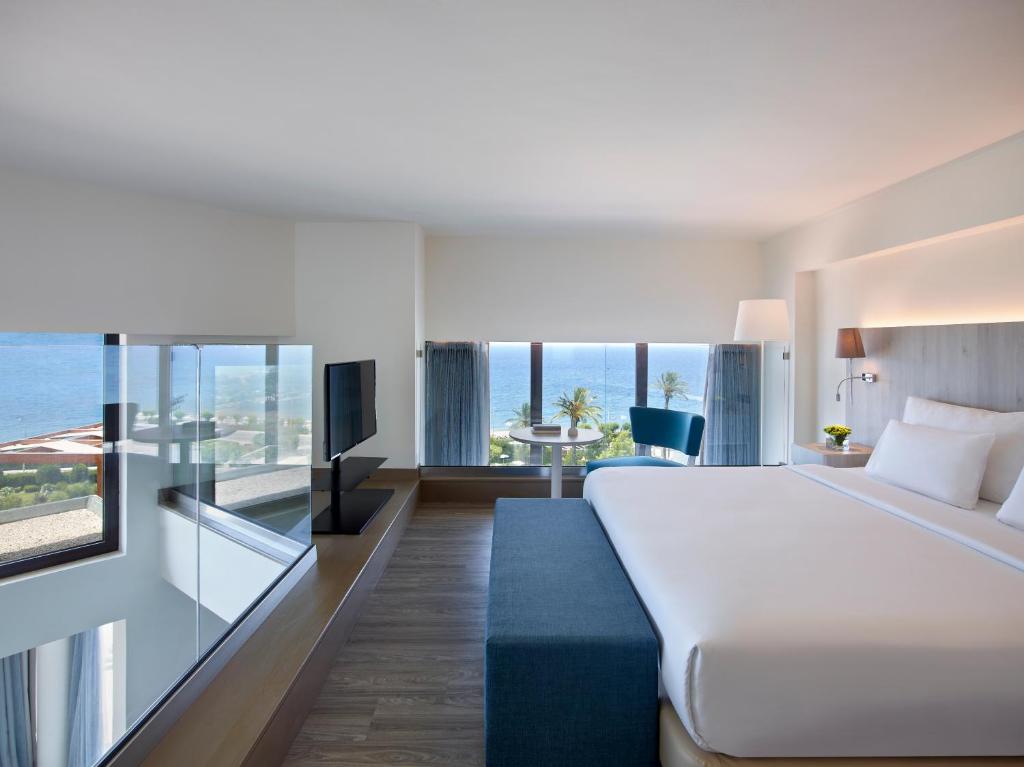 Mūsdienīga viesnīcas numura interjers ar skatu uz jūru, ietver gultu, televizoru un ērtu sēdvietu. Numurā ir lieli logi, kas nodrošina dabisko apgaismojumu un gaisīgu atmosfēru.