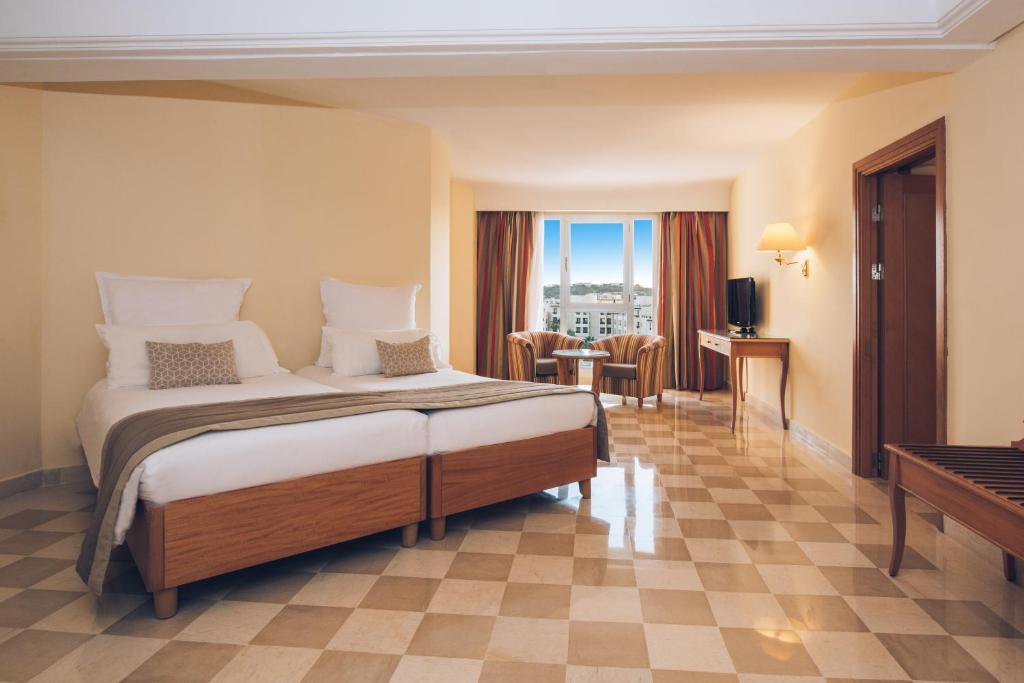 Mūsdienīga viesnīcas istaba ar divām gultām, ērtu atpūtas stūri un logiem, no kuriem paveras skats uz ārpusi. Telpa ir gaiša un plaša, ar elegantu grīdas segumu.