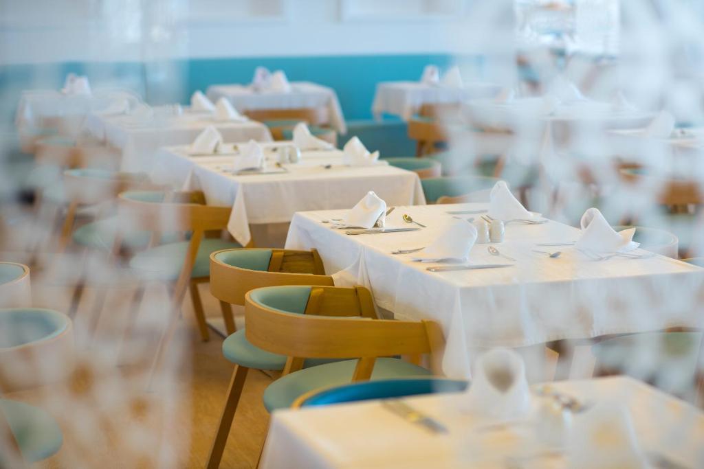 Gaiša un moderna restorāna telpa ar baltiem galdiem, dekorētiem ar salvetēm un galda piederumiem, gaida viesus. Koka krēsli ar gaiši zilu polsterējumu piešķir telpai viesmīlīgu atmosfēru.